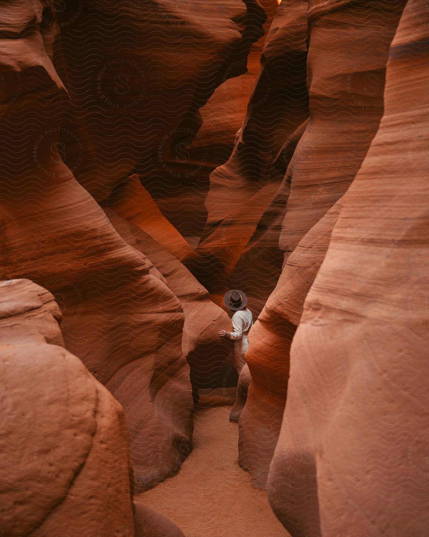 A tourist wearing a hat looks up while hiking in a narrow red rock canyon.