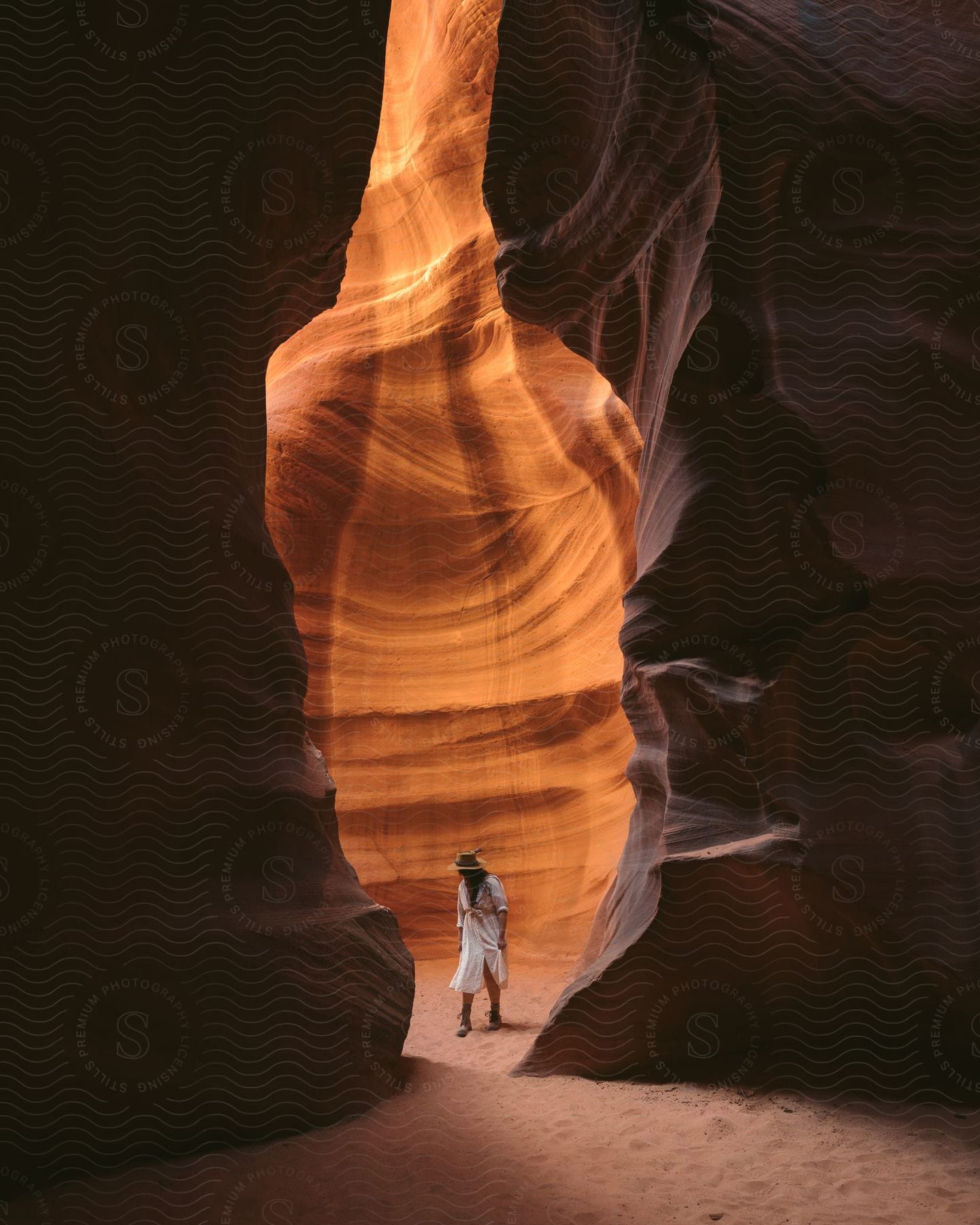 a woman wearing a white dress and a hat standing in a slot canyon