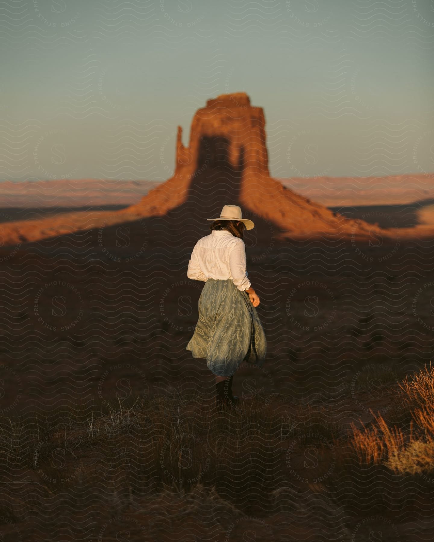 A woman wearing a hat watches the monument valley rocks during sunset.