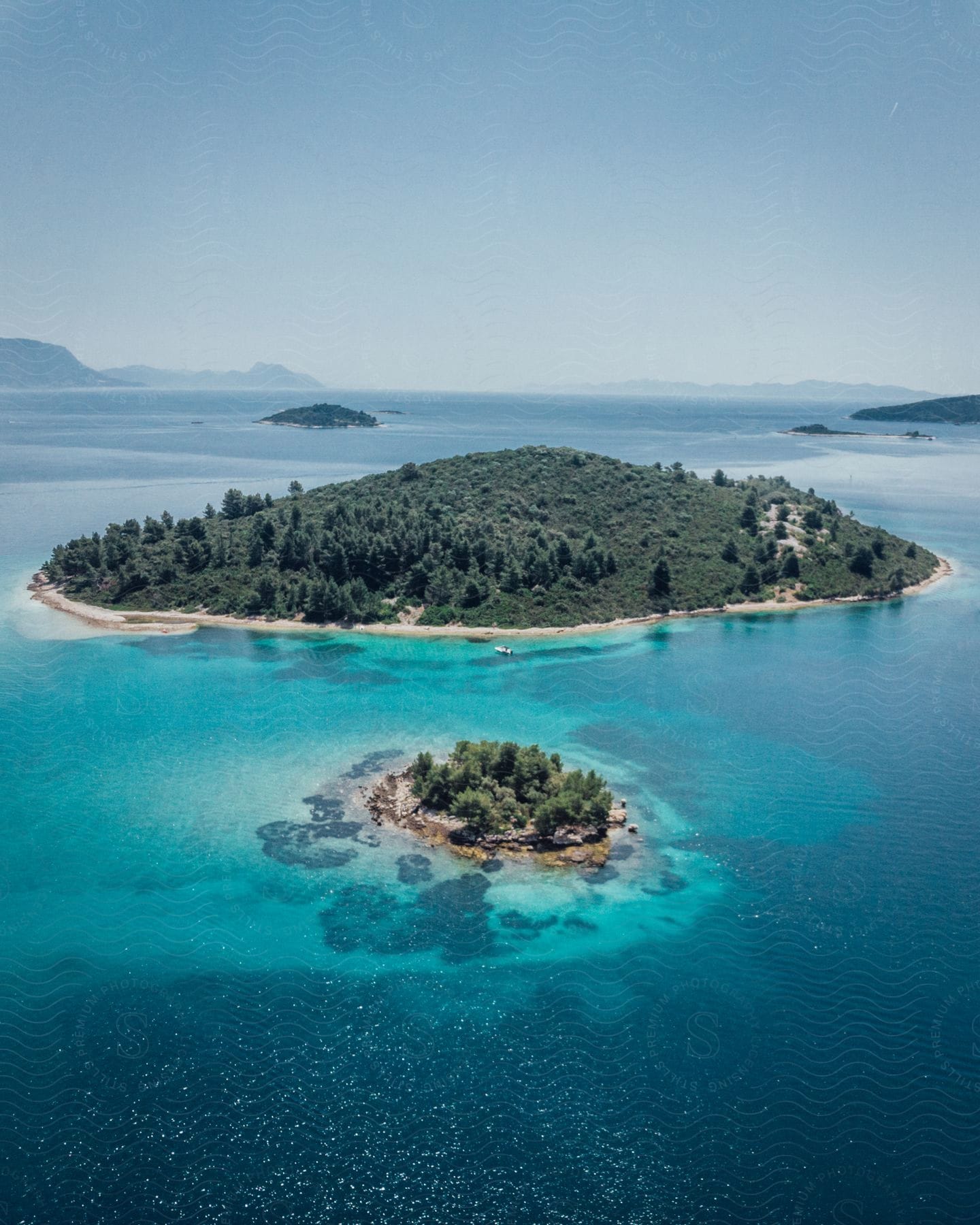 Woods cover multiple islands in blue water between coasts on hazy day.