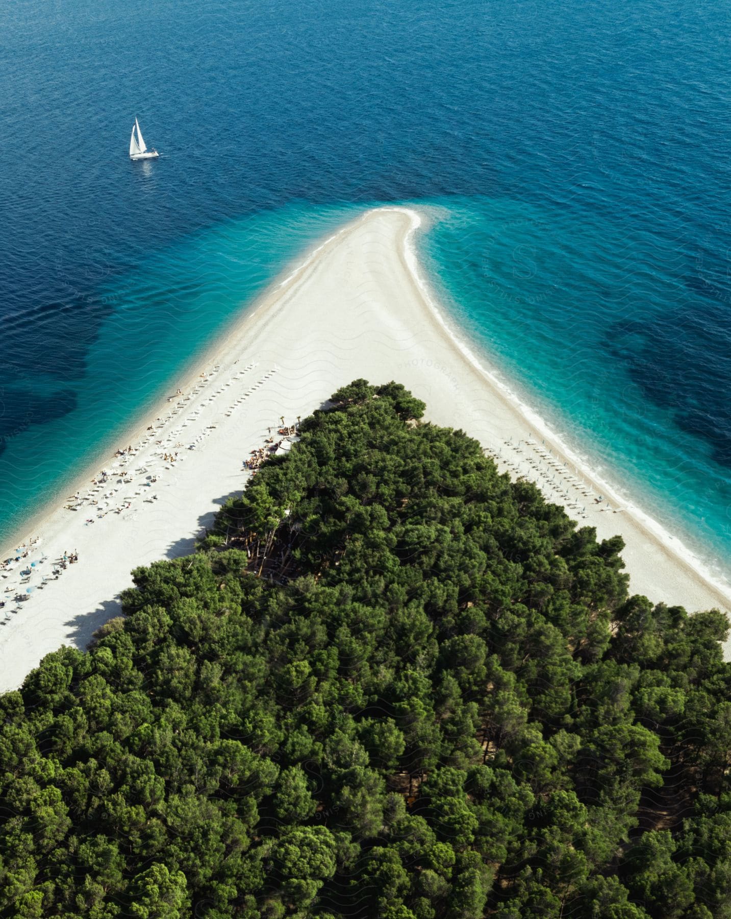 A sailboat sails above a beach promontory.