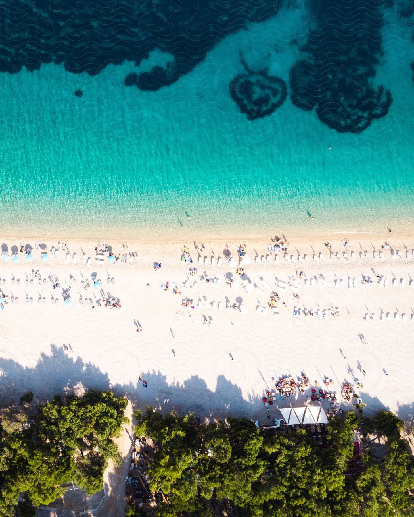 Looking down at many people on a beach between the clear blue water and trees