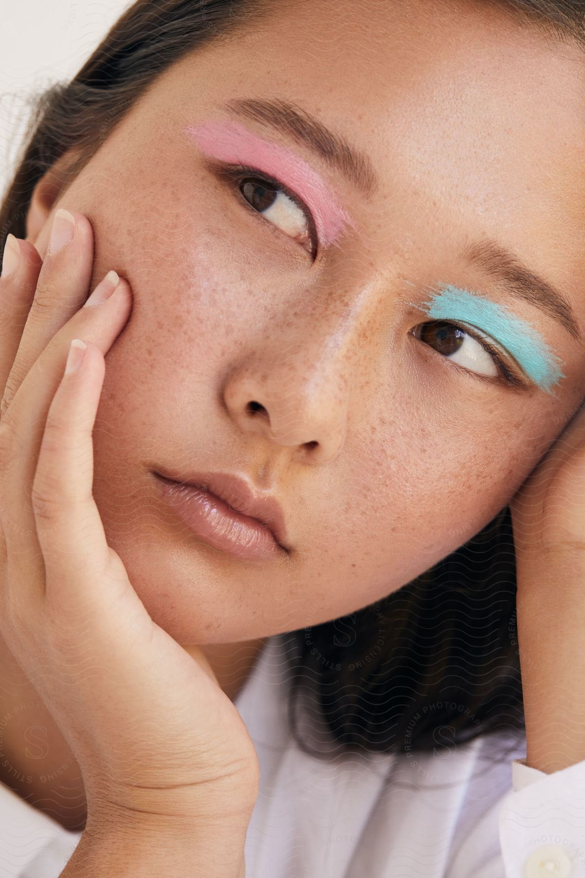 A young Asian woman with freckles has two different colors of bright eye shadow applied over each eye.