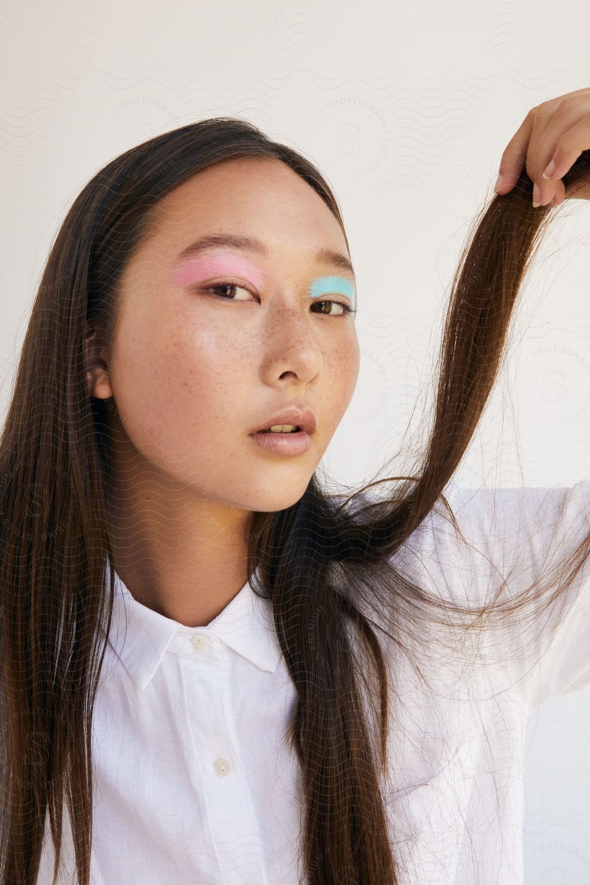 A young woman holds up her long brown hair in her hand