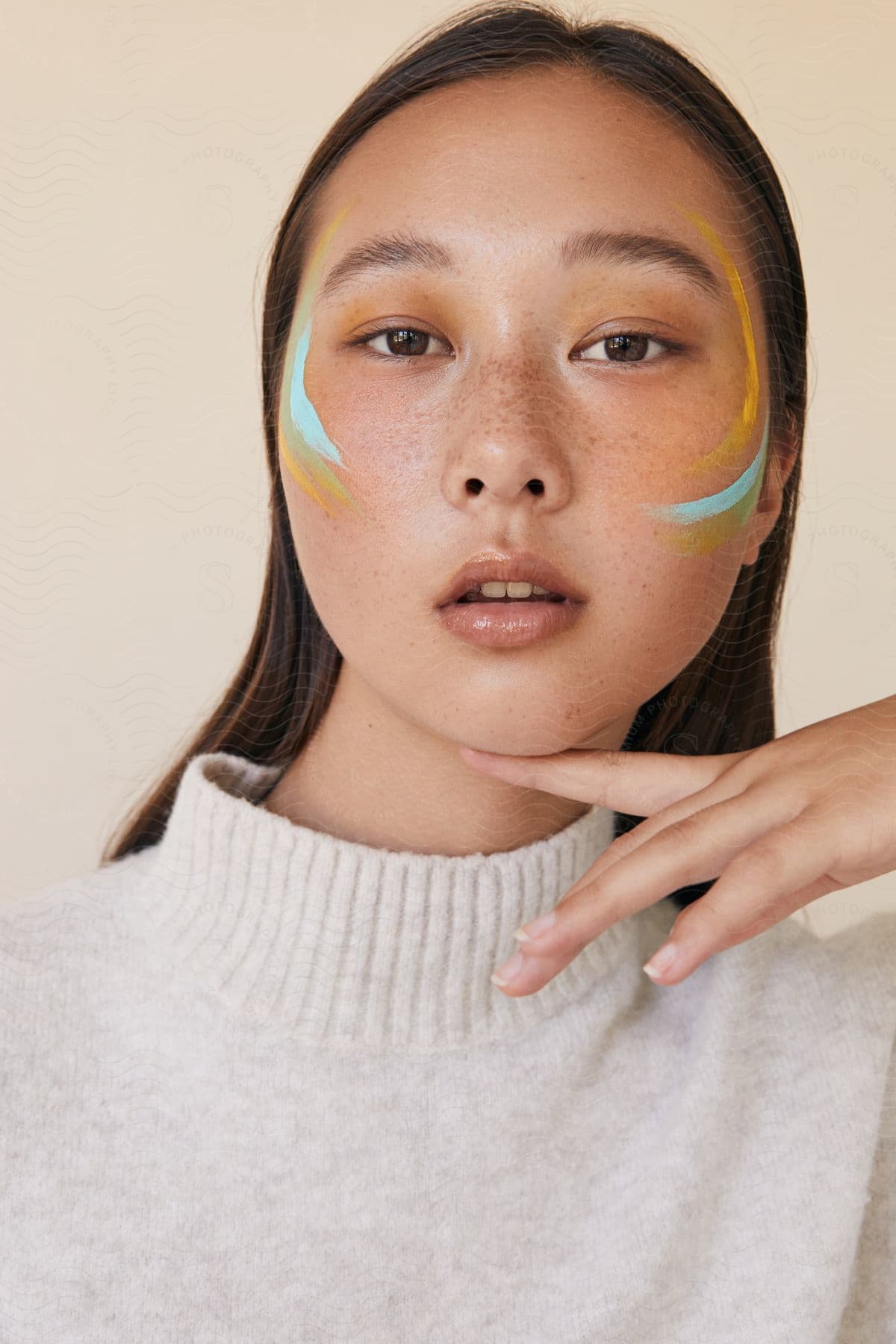 a young Asian teen drawing paint on her face with her finger placed under her chin