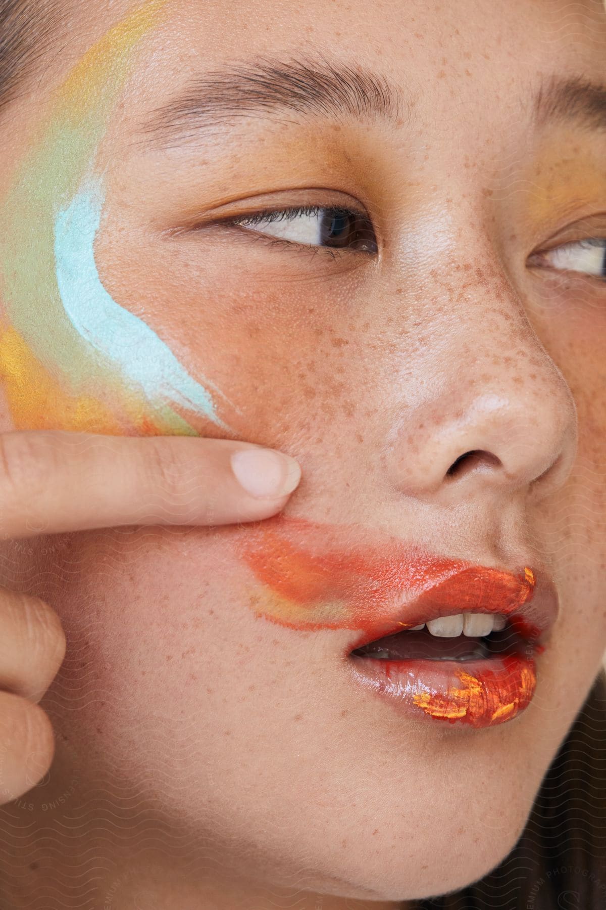 Asian girl with paint on her freckled face, temples and lips looks to the side while posing.