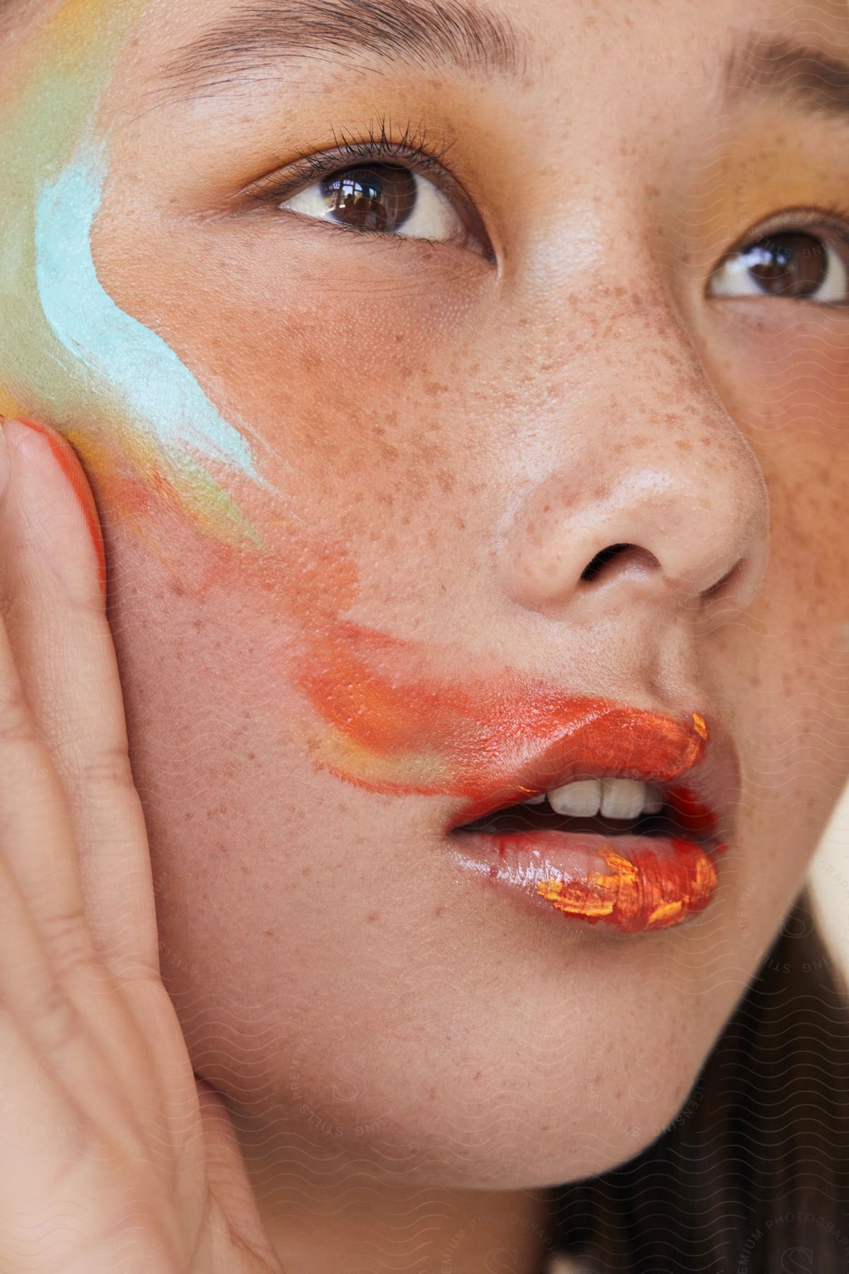 A young woman looks up as she smears makeup on her face and lips with her hand