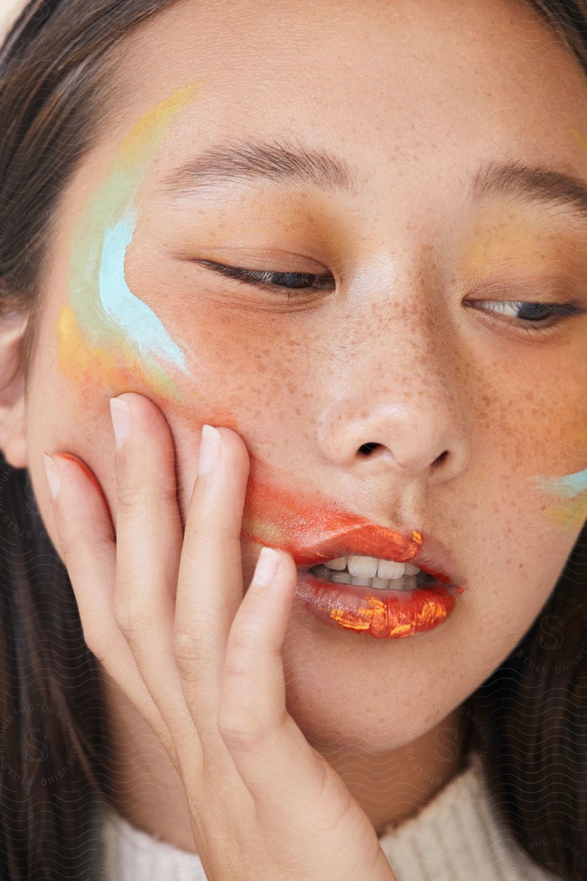 Asian teen with freckles and paint on her face posing in a pensive mood.