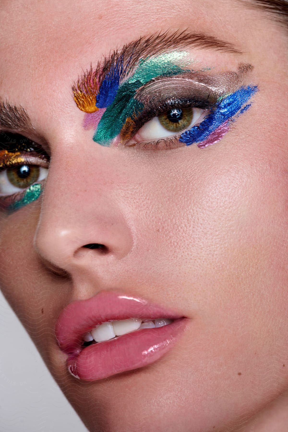 Close-up on a woman's face with glossy lips and multicolored eye makeup.