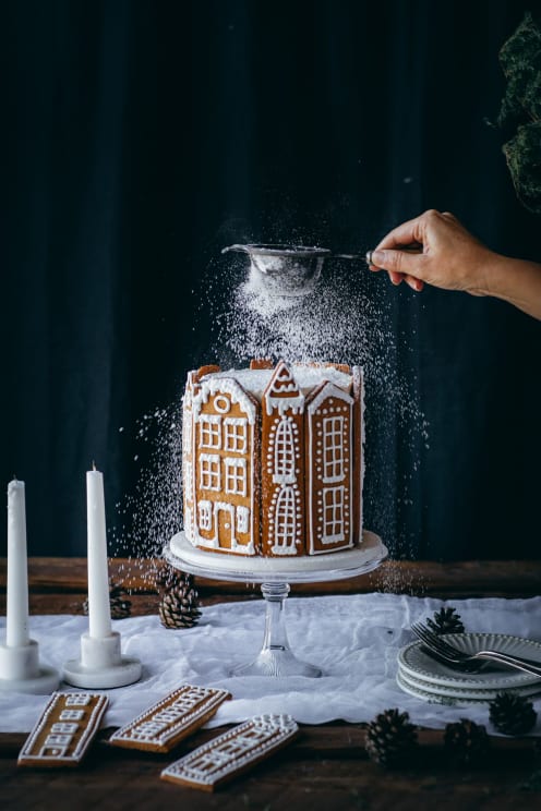 Woman Sprinkling Sugar On A Gingerbread Village Cake