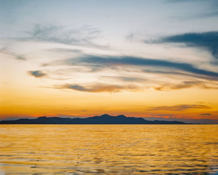 Seascape With Mountains On The Horizon And An Orange Sunrise Sky