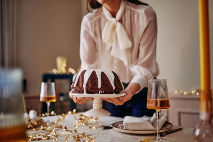 A Person Wearing Pink Clothing Holding A Chocolate Cake On A Table;