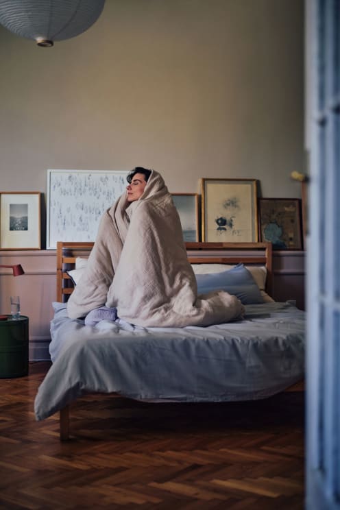 A Woman Sitting In Bed Wrapped In A Blanket
