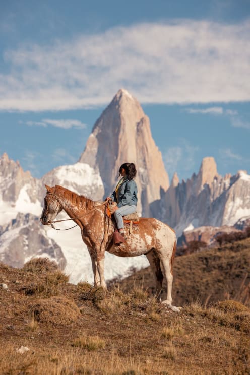 A Woman Sits On Her Horse On A Mountain With Mountains In The Distance