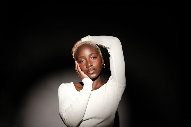 A Woman With Short Hair, Earrings, And A White Sweatshirt Strikes A Pose For The Camera In The Spotlight