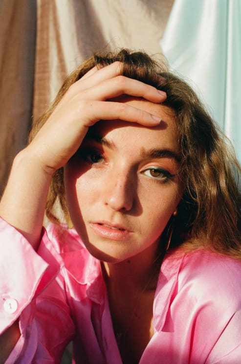 A Woman Wearing A Pink Blouse Sits With Her Hand On Her Head