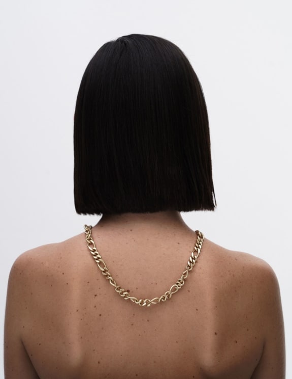 Woman Standing With Her Back Turned And Black Hair Cut Straight With A Gold Necklace On Her Back