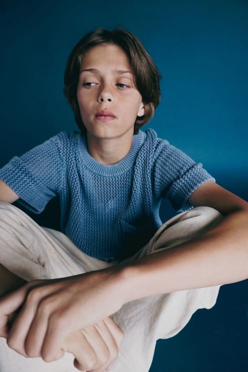 Young Model Boy Sitting Posing In A Blue Shirt And Beige Pants