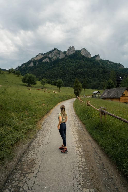 A Woman Standing In The Middle Of A Rural Road, Looking At The Pasture And Mountains Ahead
