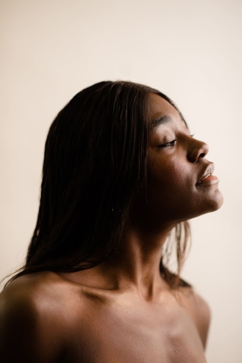 Side Portrait Of A Shirtless Young Black-haired Woman On A White Blurred Background