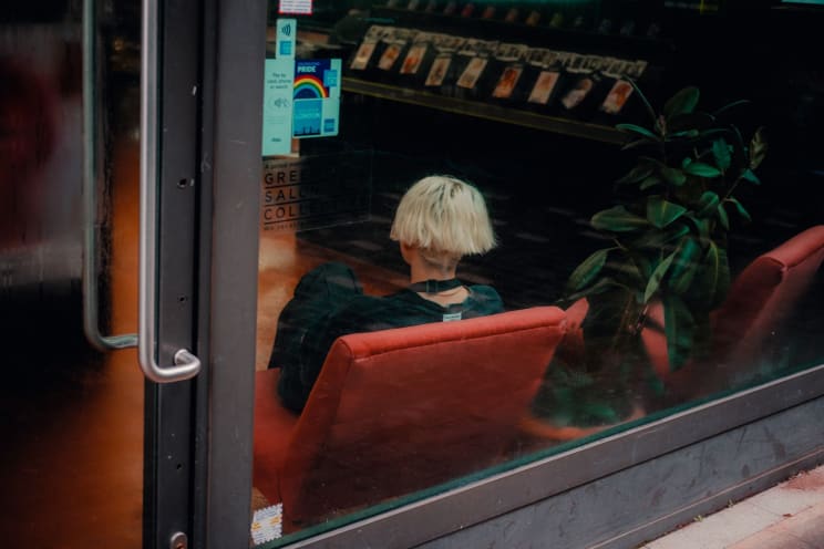A Blonde Woman Sits On A Red Chair Inside A Business