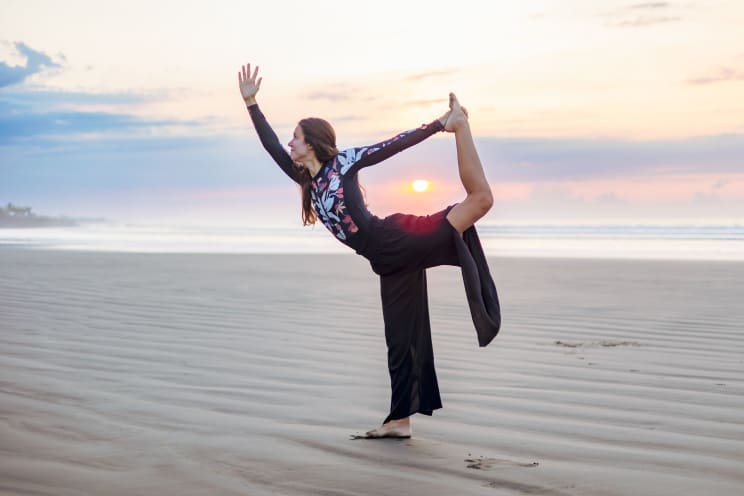 Woman In Yoga Position Standing On The Beach Sand With A Sunset On The Horizon