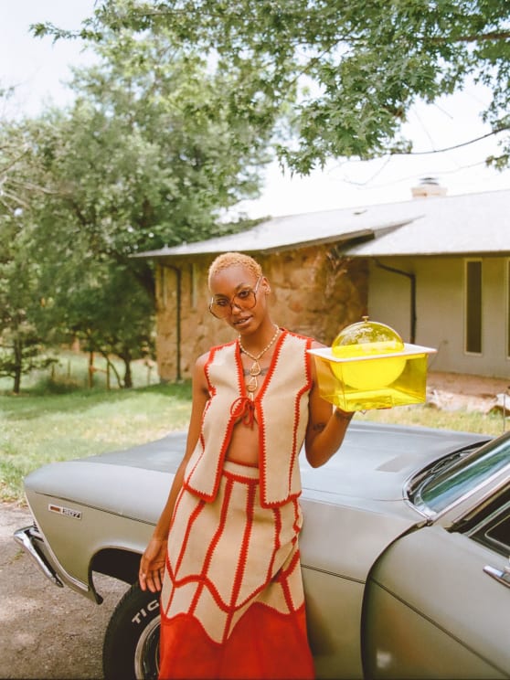 Woman Standing Next To Her Car In A Neighborhood Holding A Yellow Glass Container