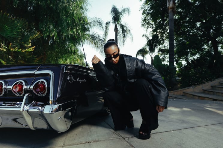 Female Wearing Leather Jacket And Sunglasses Crouching Next To A Car Posing Outdoors