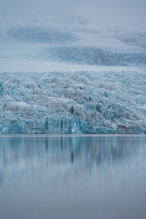 Blue Glacier Ice Reflects Off Body Of Water Below