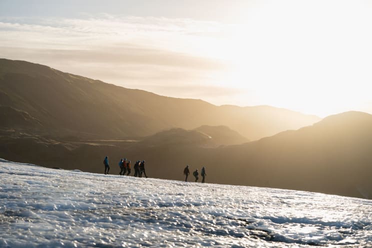 Mountain Covered In Snow With People Hiking In The Morning And Silhouettes Of Other Mountains On The Horizon