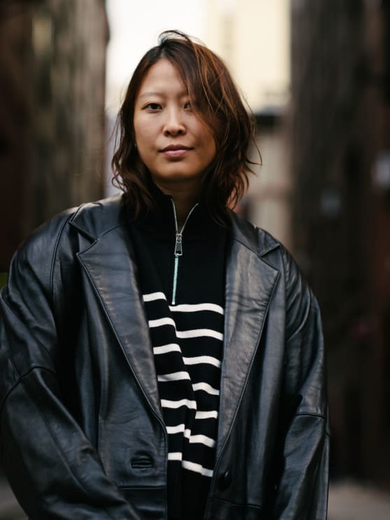 Woman With Shoulder-length Hair Wearing A Black Leather Jacket And A Striped Sweater