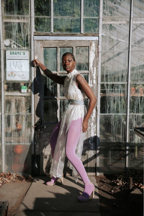 Woman In A White Dress And Pink Pants In Front Of The Entrance To A Greenhouse
