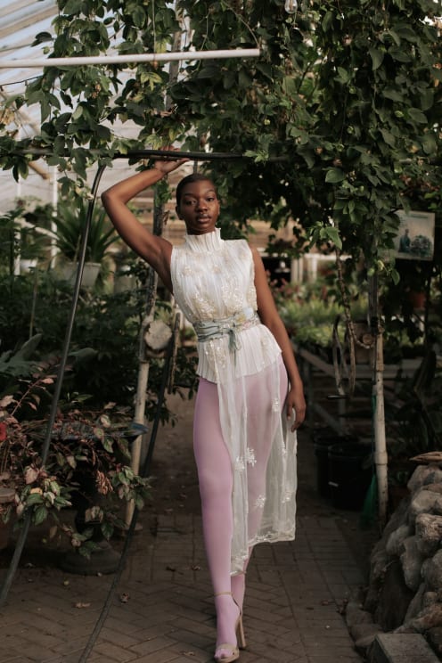 Woman Model Wearing A White Dress And Pink Leggings In A Greenhouse With Plants