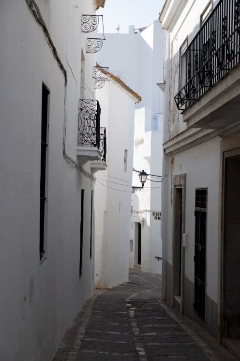 A Narrow Alley With Whitewashed Buildings And Wrought-iron Balconies
