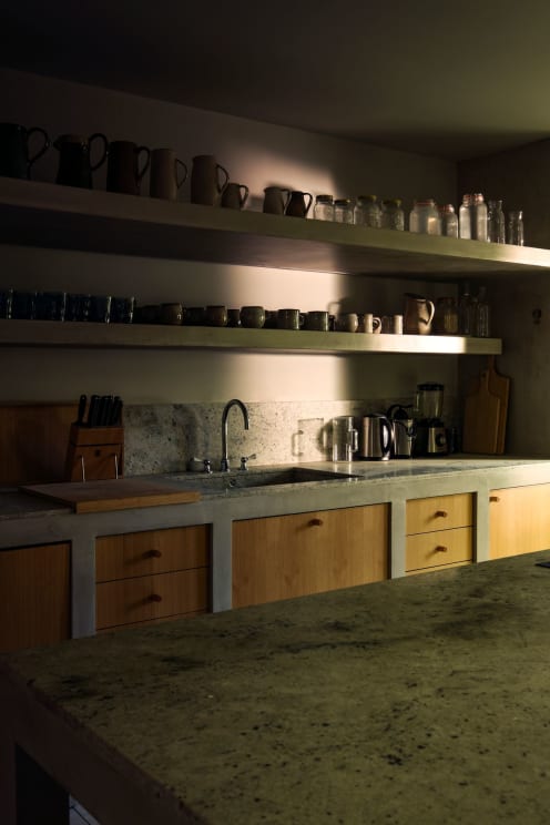 A Dark Kitchen With A Marble Centerpiece And Shelves Filled With Coffee Bottles
