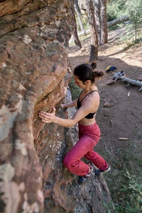 A Woman In A Black Top And Pink Pants Is Climbing A Stone Wall