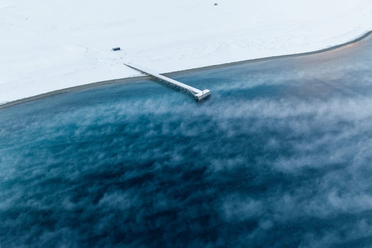 White Pier Stretching Into A Blue Lake Surrounded By A Snow-covered Landscape