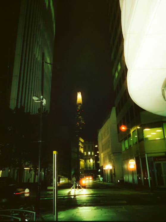 Cars Drive Down The Street While Pedestrians Walk Across An Intersection In An Urban Area At Night