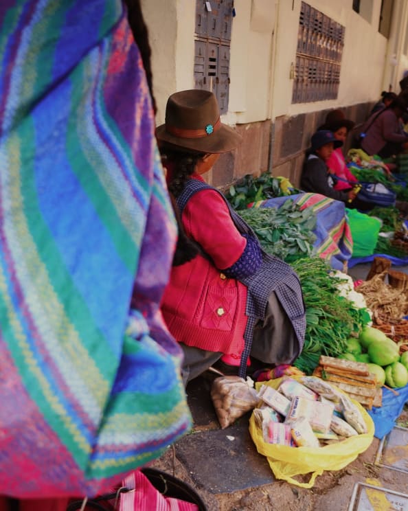 People Sitting At An Open-air Market, Selling A Variety Of Vegetables And Other Items