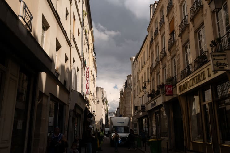 Urban Street With Pedestrians And Commercial Stores Around Against A Cloudy Sky