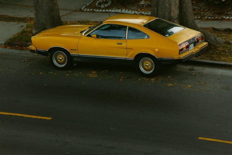 Vintage Yellow Car With A Black Vinyl Roof Parked On A Tree-lined Street