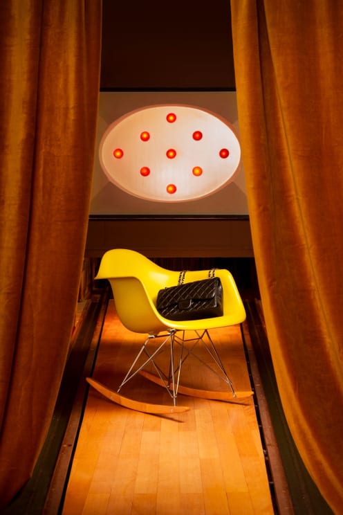 A Room With A Wooden Floor Contains A Yellow Rocking Chair With A Black Purse Sitting On It