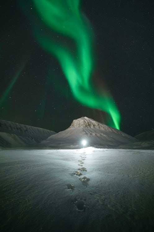 Landscape Of Mountains Covered By Snow And The Sky With Greenish Northern Lights