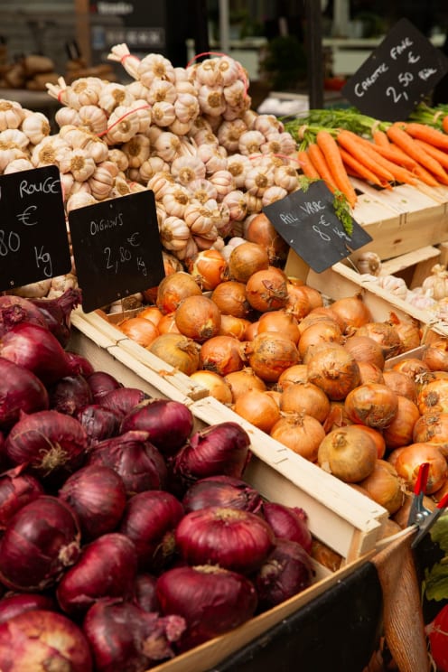 Variety Of Fresh Vegetables Such As Garlic, Onions And Carrots Arranged In Wooden Boxes In A Market