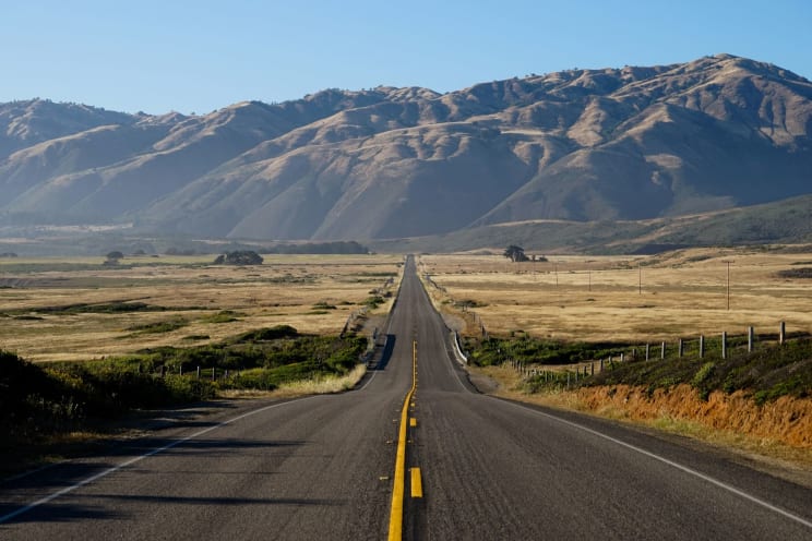 Open Road Through Rural Land Leading To Mountains