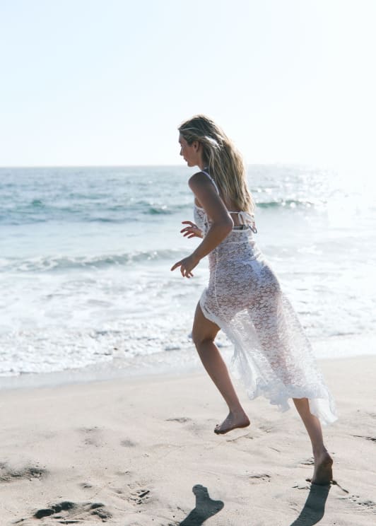 A Blond Woman In A Sheer Dress And White Bikini Running On The Beach