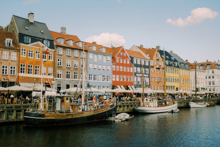 Colorful Buildings And Boats Along A Lively Canal In A European City With People Dining At Outdoor Cafes