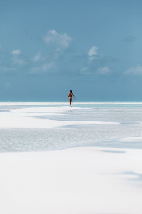 A Woman Walking Towards The Sea On A White Sand Beach