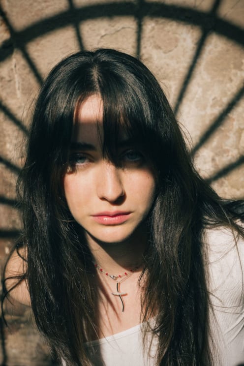 Young Woman With Long Dark Hair Against A Stone Wall With Shadow Patterns On Her Face