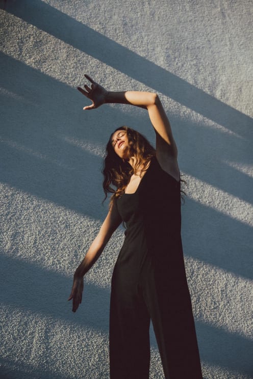 A Woman Wearing A Black Dress Standing Next To A Wall With Sunlight Reflecting On Her
